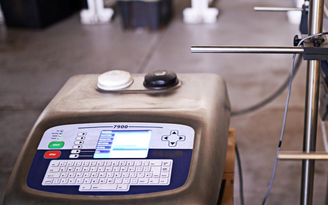 Close-up of an industrial control machine with a keyboard and display screen in a factory setting.